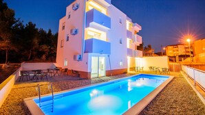Un edificio moderno con piscina, mobiliario exterior y una entrada bien iluminada.