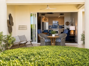 An open-plan living area with a dining table, two chairs, a sofa, and a kitchen in the background.