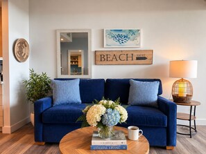 Un sofá azul con cojines, un florero con flores, una taza de café y un letrero enmarcado que dice 'BEACH 500 FT'.