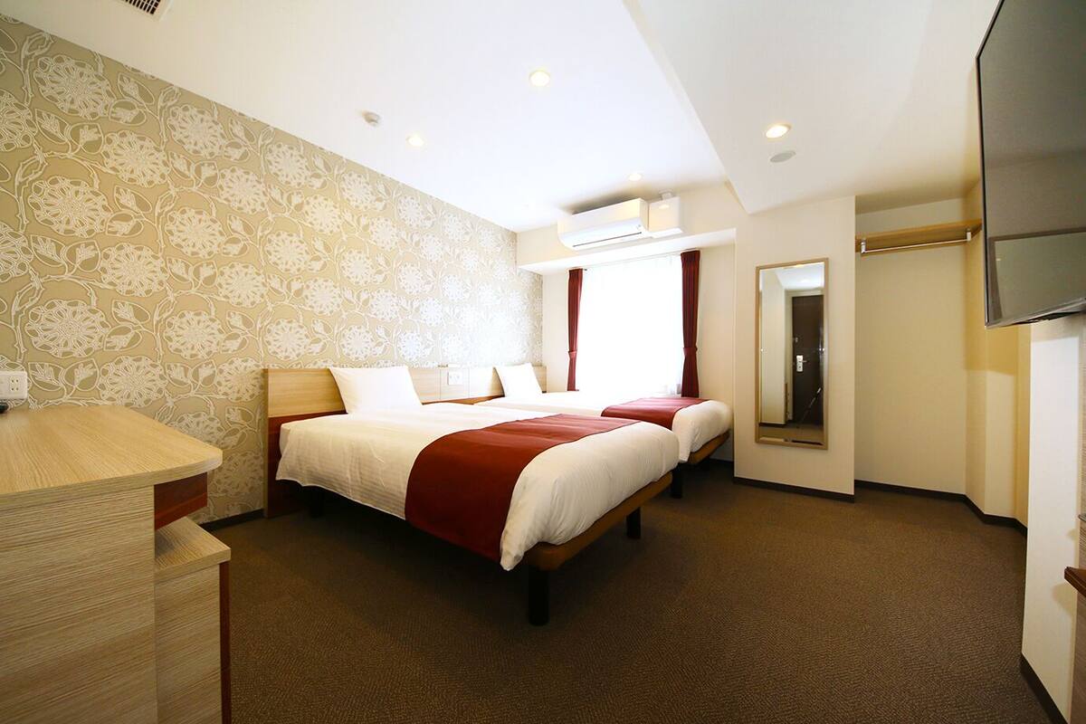 A hotel room with two beds, a desk, a mirror, and a TV.