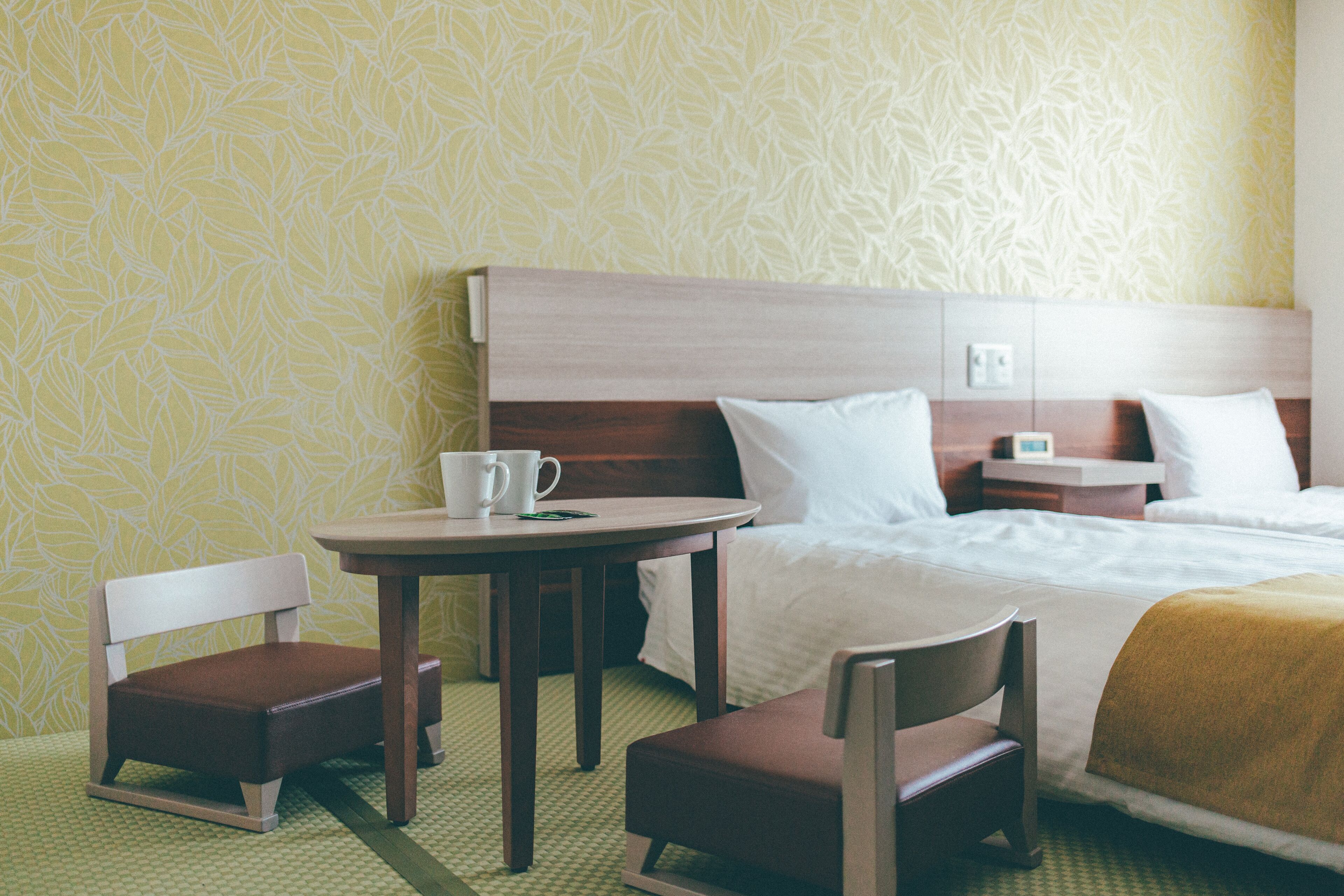 Habitación de hotel con una cama, una mesita de noche con una taza, una silla y una lámpara.