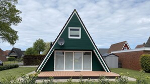 Ein modernes, dreieckiges Haus mit grüner Fassade, einem kleinen Fenster und einer Satellitenschüssel.