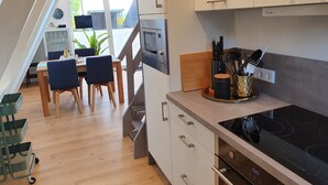 Eine moderne Küche mit Einbauherd, ein Essbereich mit Tisch und Stühlen sowie eine Treppe, die in ein Obergeschoss führt.