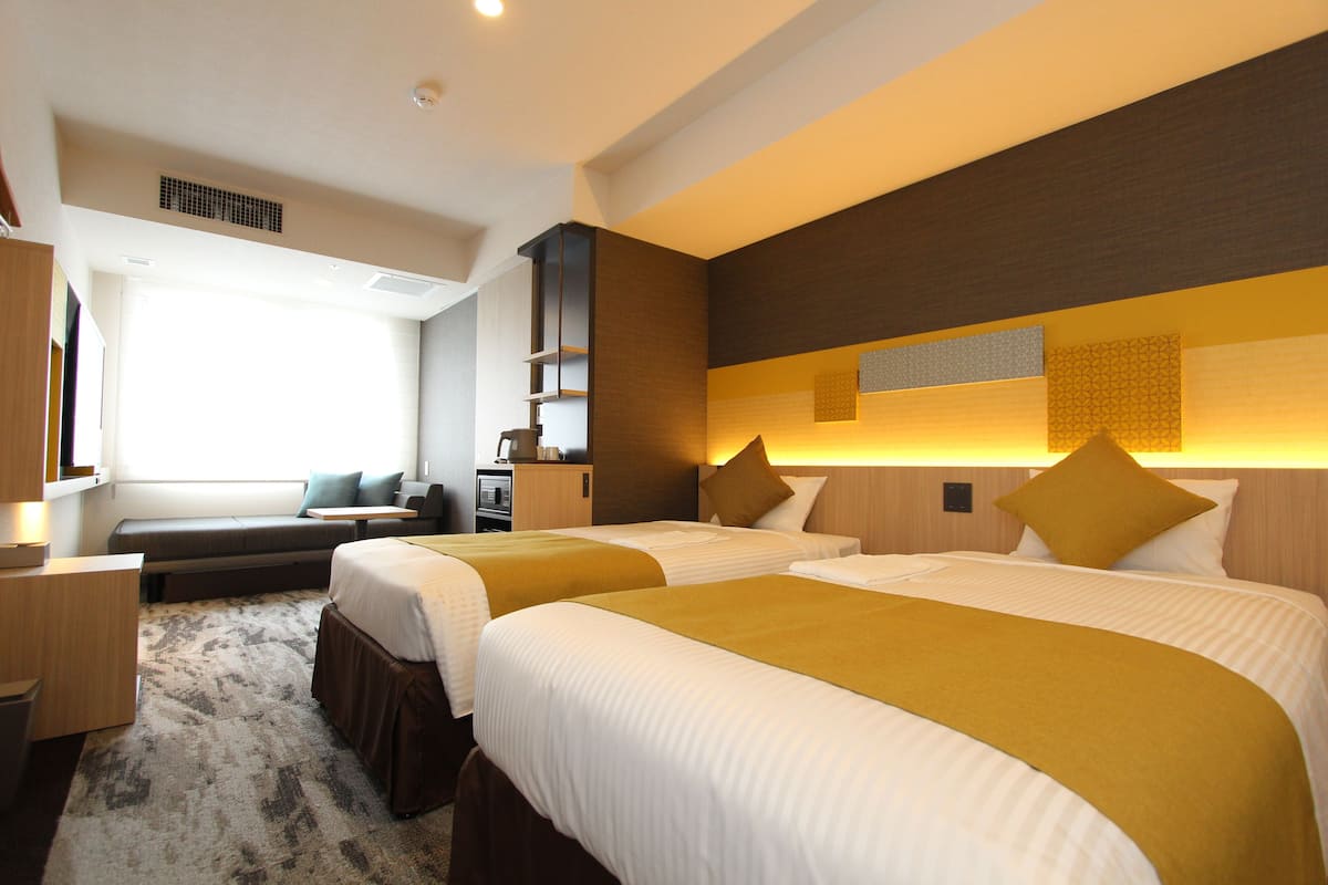 Une chambre d’hôtel avec deux lits, un canapé, un bureau et une grande fenêtre.