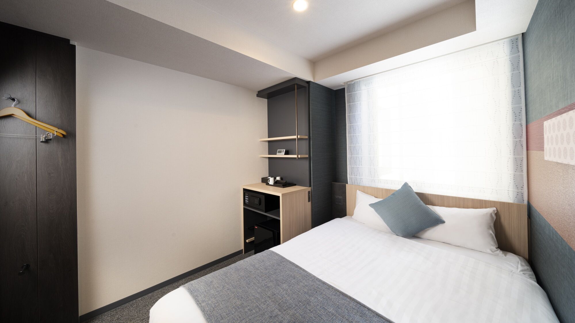 Une chambre d’hôtel avec un lit, une armoire, un bureau avec un téléphone et une fenêtre avec des rideaux.