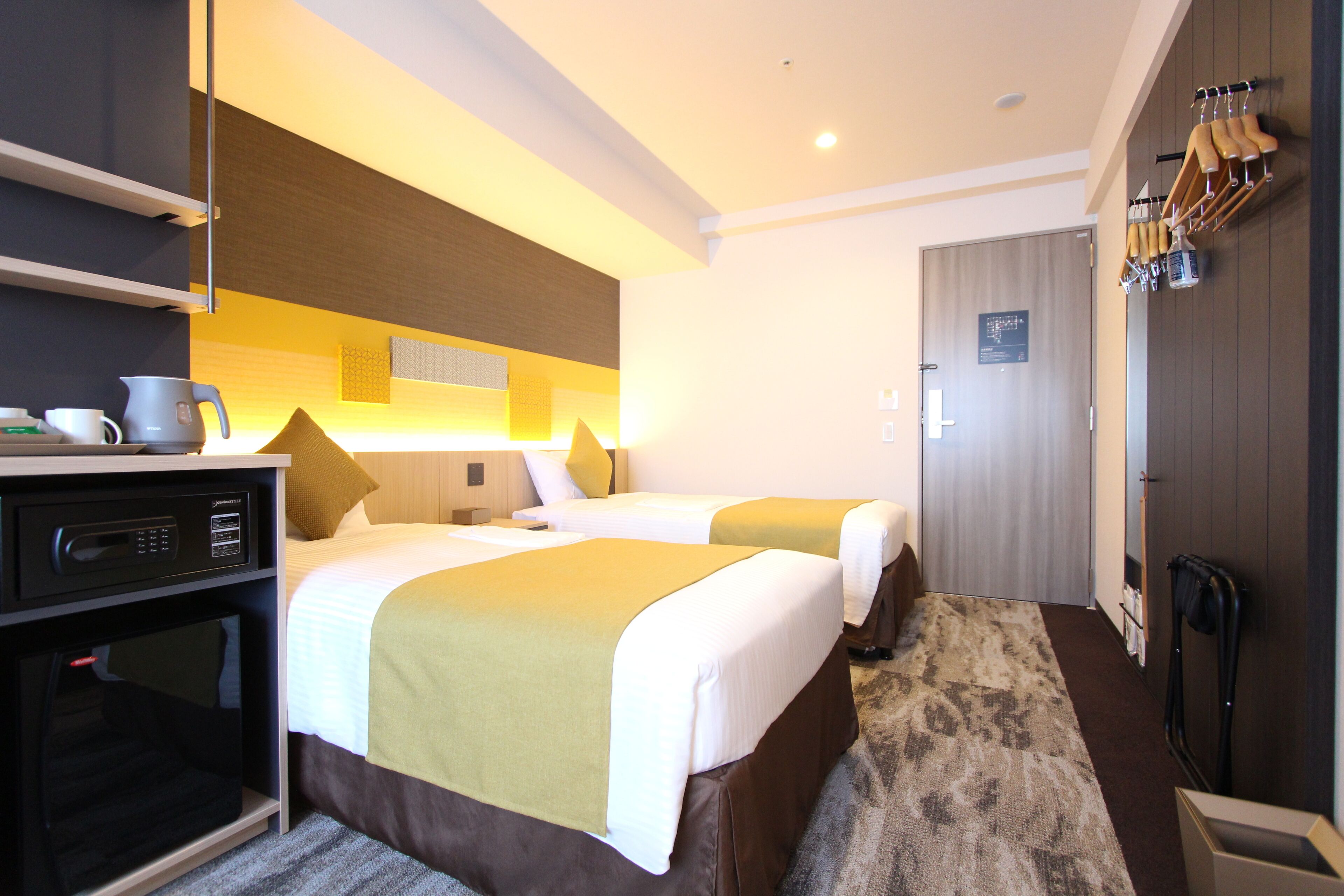 A hotel room with two beds, a desk with a microwave, a coffee maker, and a shoe rack.