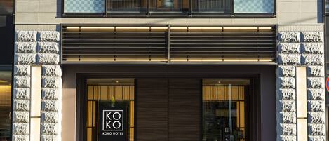 A modern hotel entrance with a prominent logo, large glass doors, and a well-lit facade.