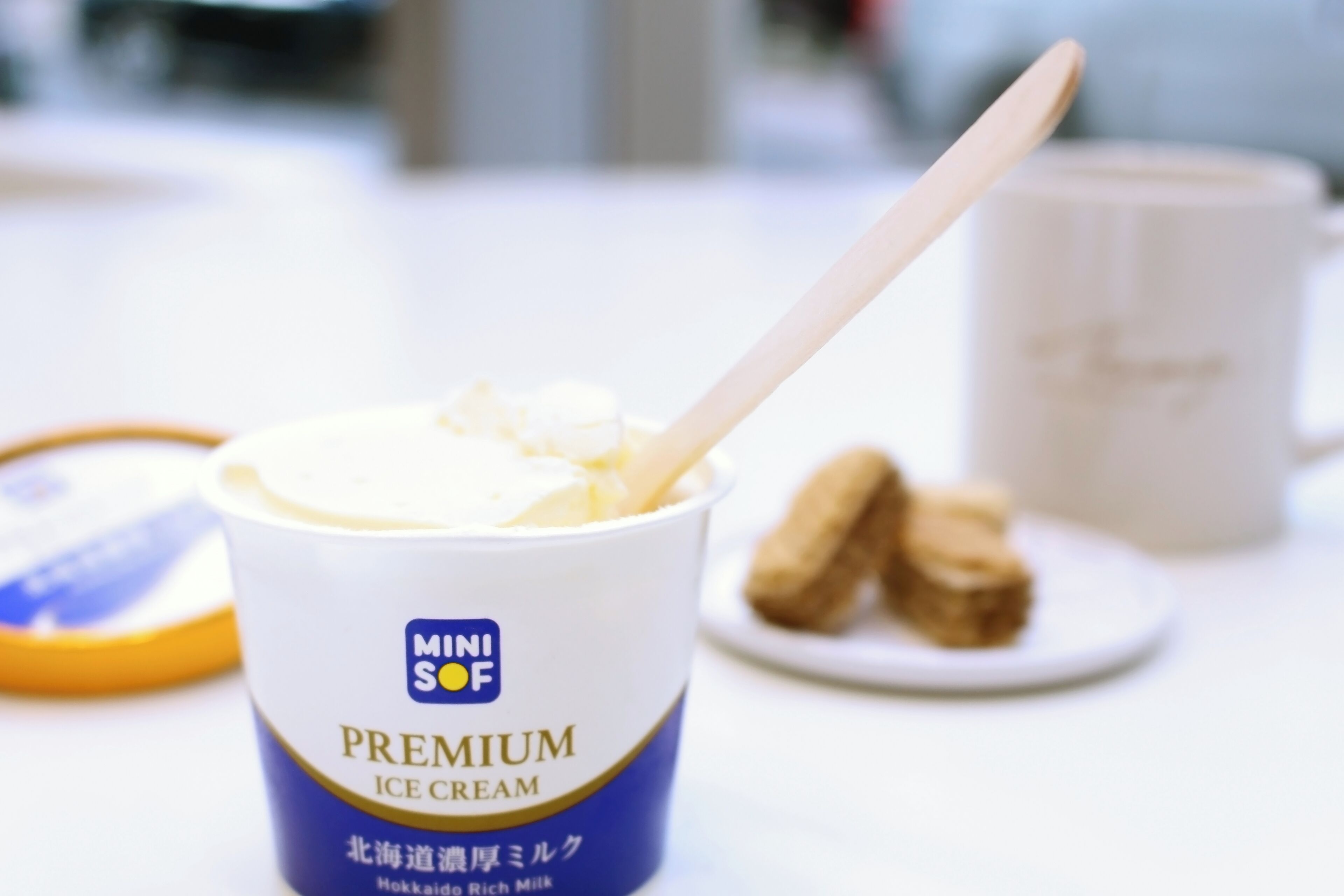 Uma taça de sorvete premium Mini SOF com uma colher, um prato de biscoitos e uma taça ao fundo.