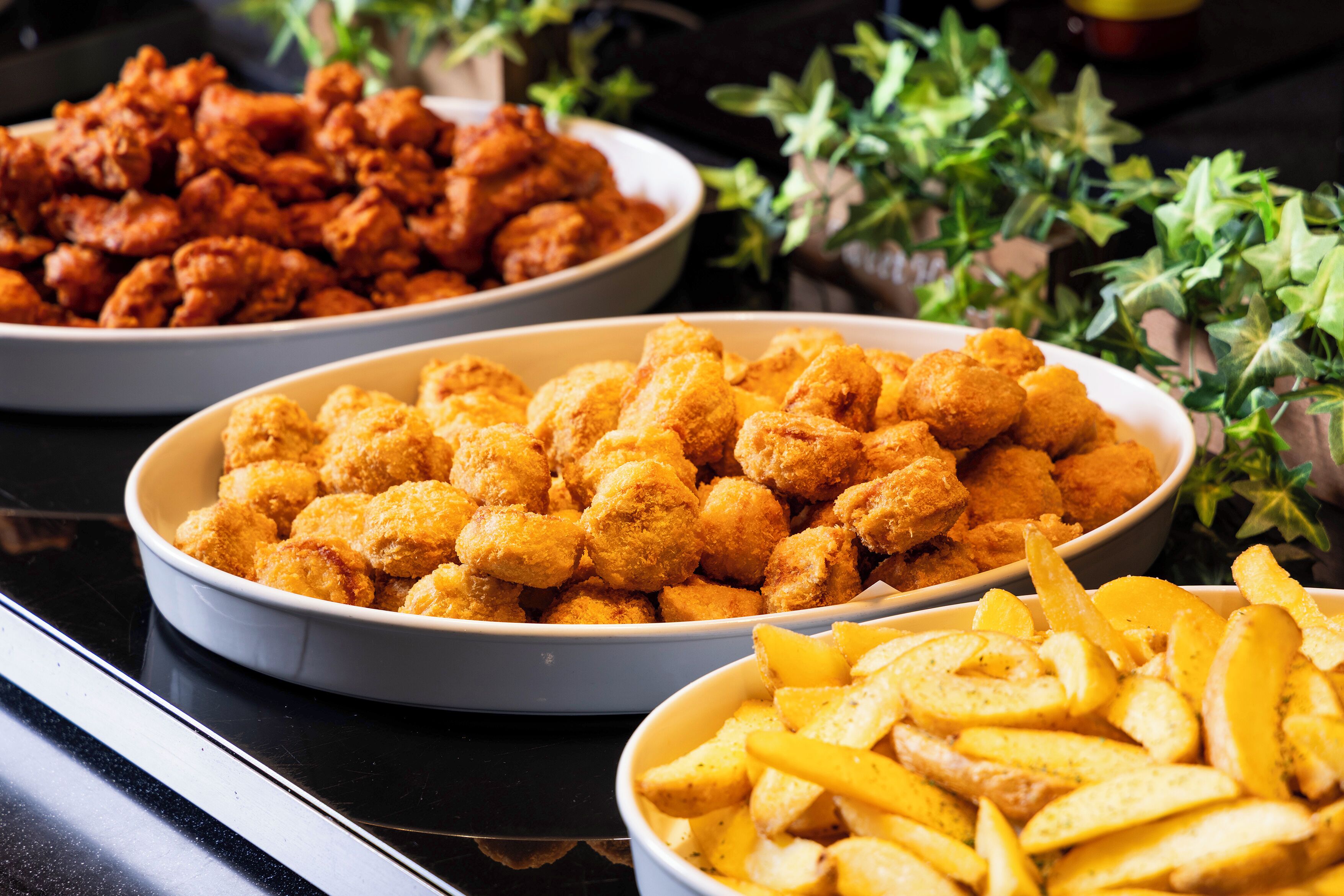 A buffet table with various dishes including fried chicken, tater tots, and French fries.