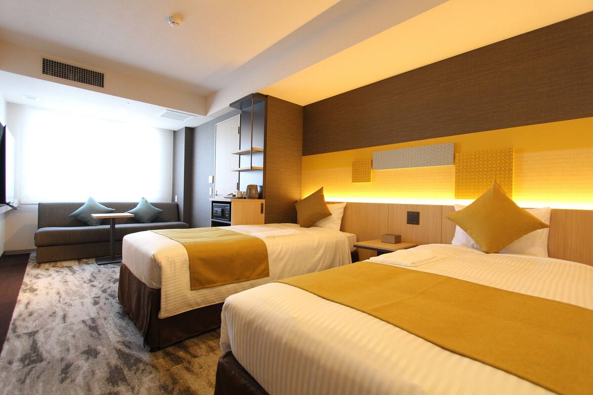 Une chambre d’hôtel avec deux lits, un canapé, un bureau et une grande fenêtre.