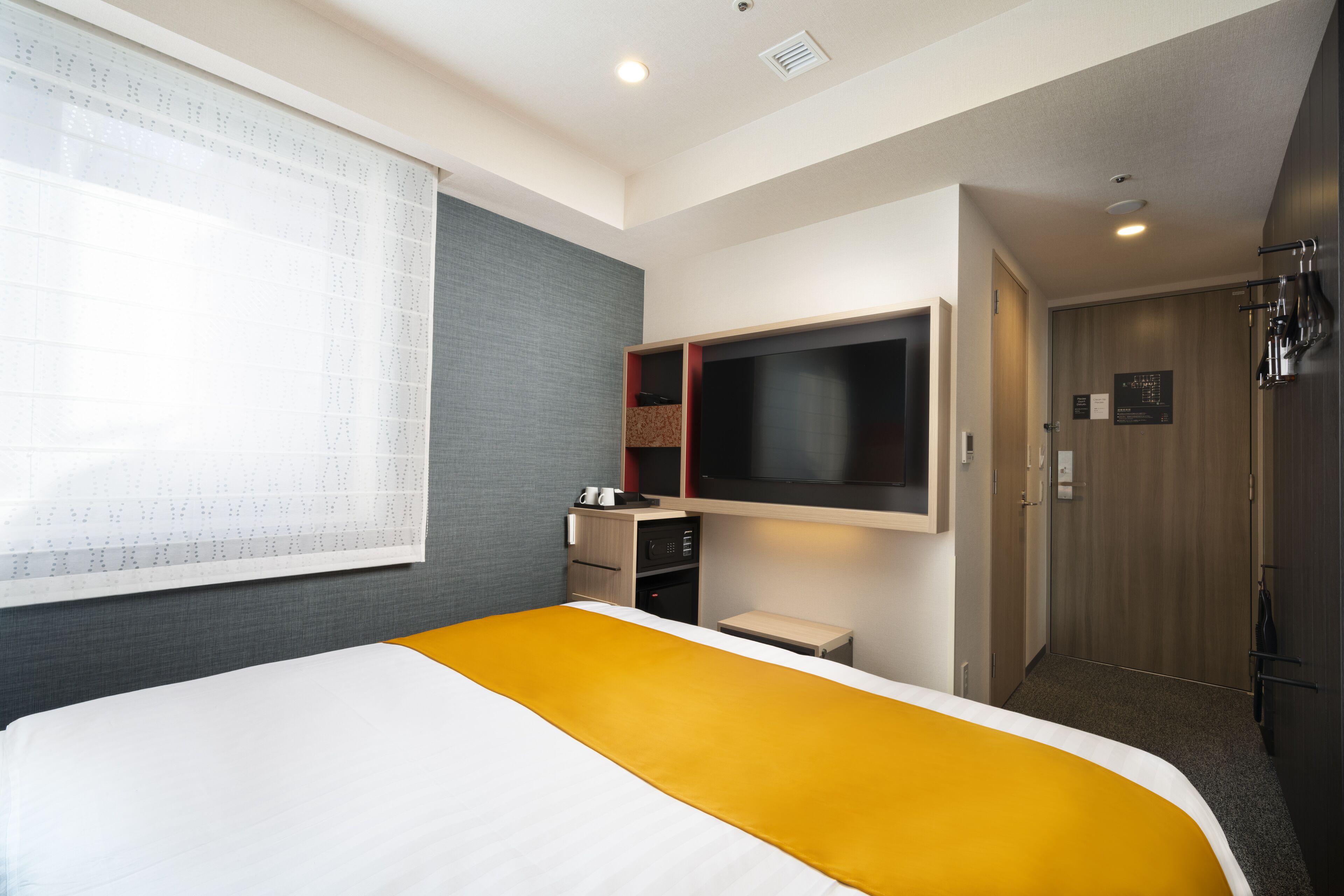 Habitación de hotel con cama, televisión montada en la pared, escritorio pequeño y armario.