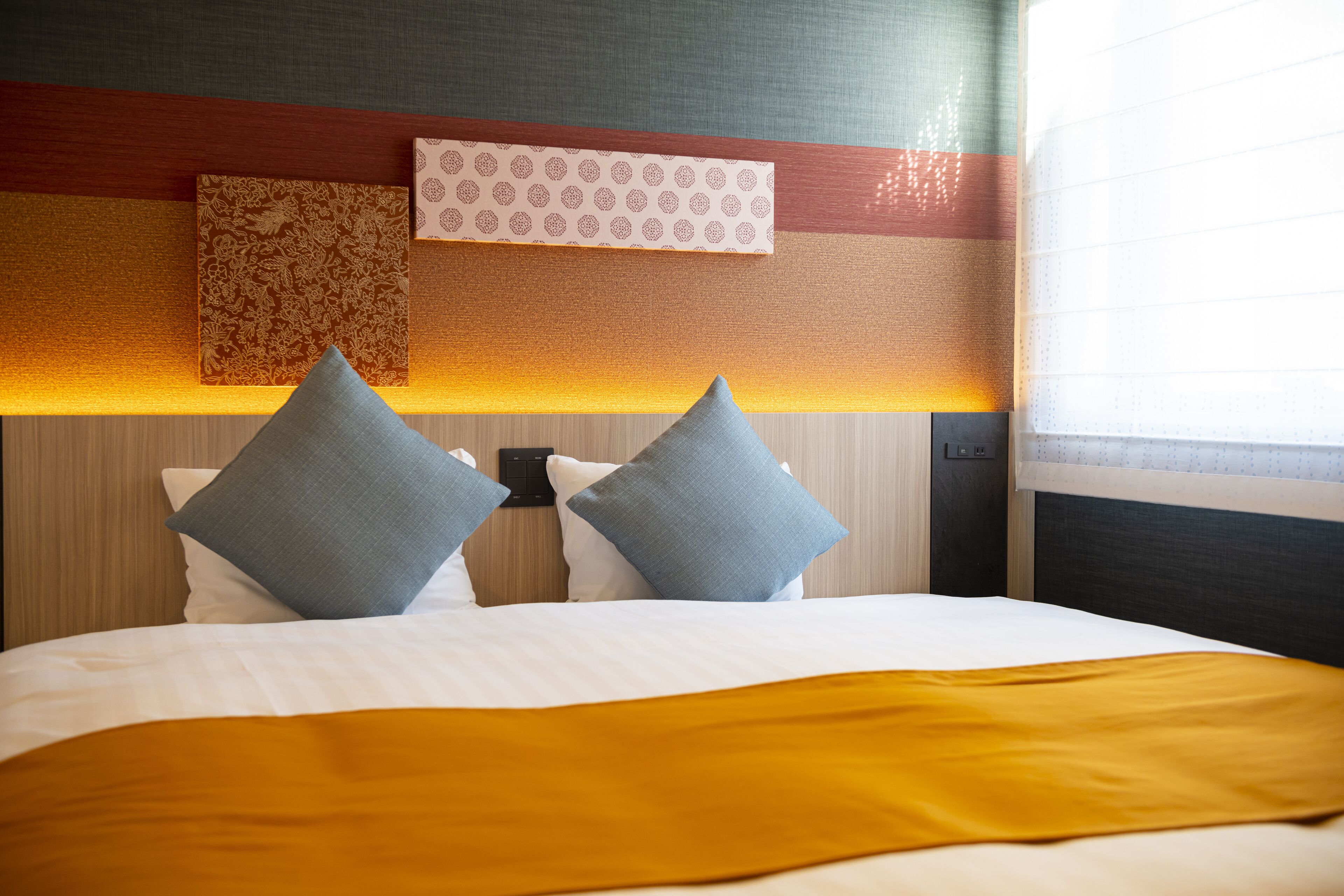 Un lit bien fait, avec deux oreillers, une table de chevet et une lampe fixée au mur.