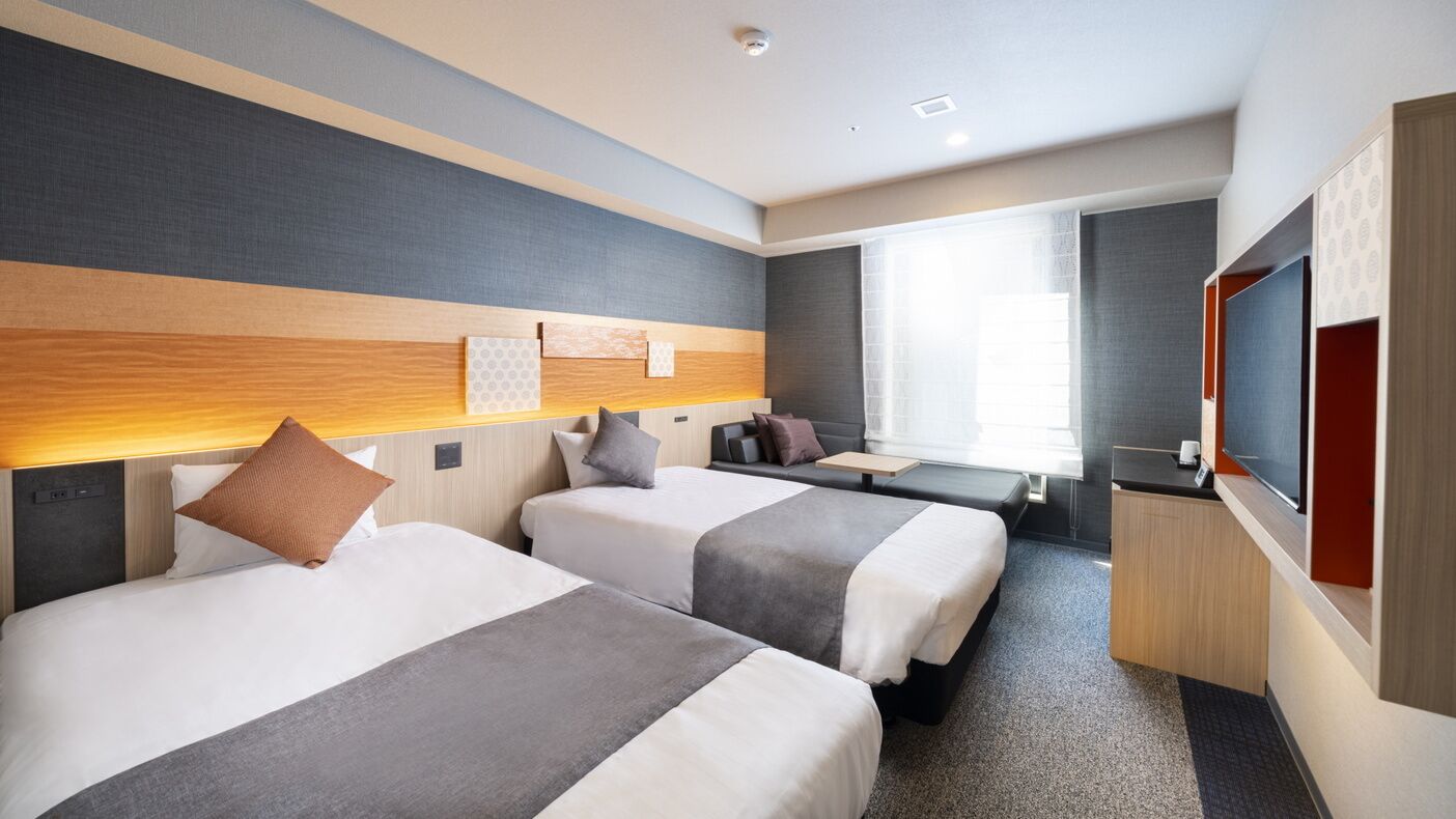 Une chambre d’hôtel avec deux lits, un bureau, une télévision et une grande fenêtre.