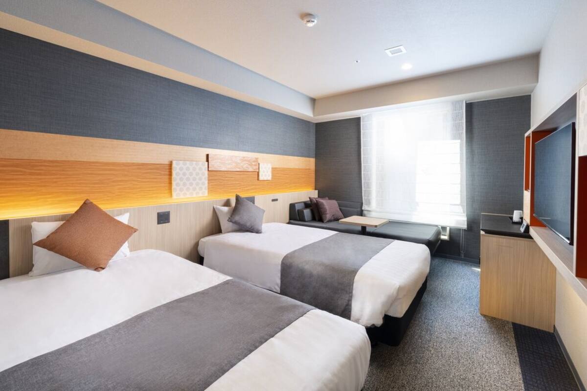Une chambre d’hôtel avec deux lits, un bureau, une télévision et une grande fenêtre.