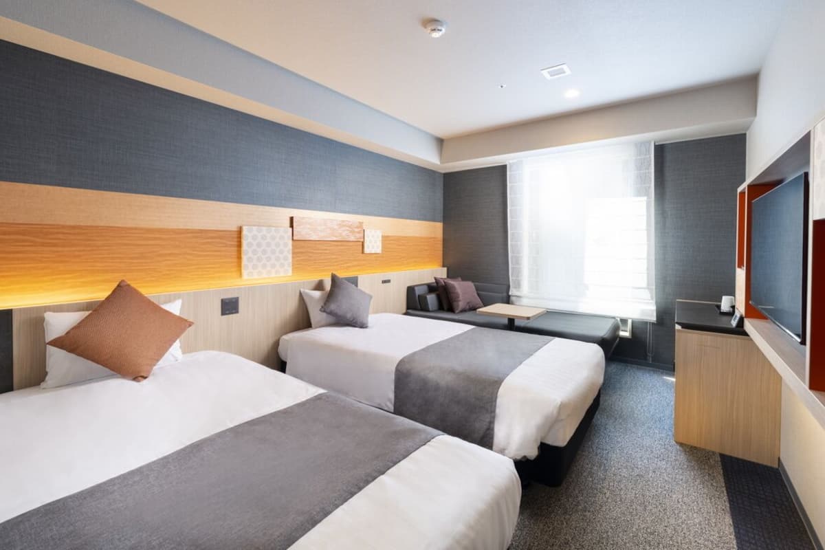 A hotel room with two beds, a desk, a TV, and a large window.