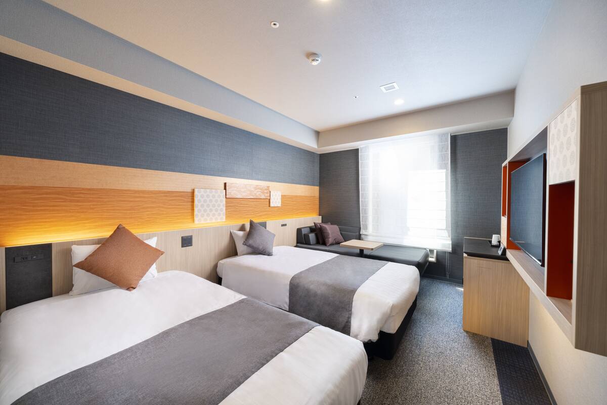 Une chambre d’hôtel moderne avec deux lits, un petit coin salon et un téléviseur.