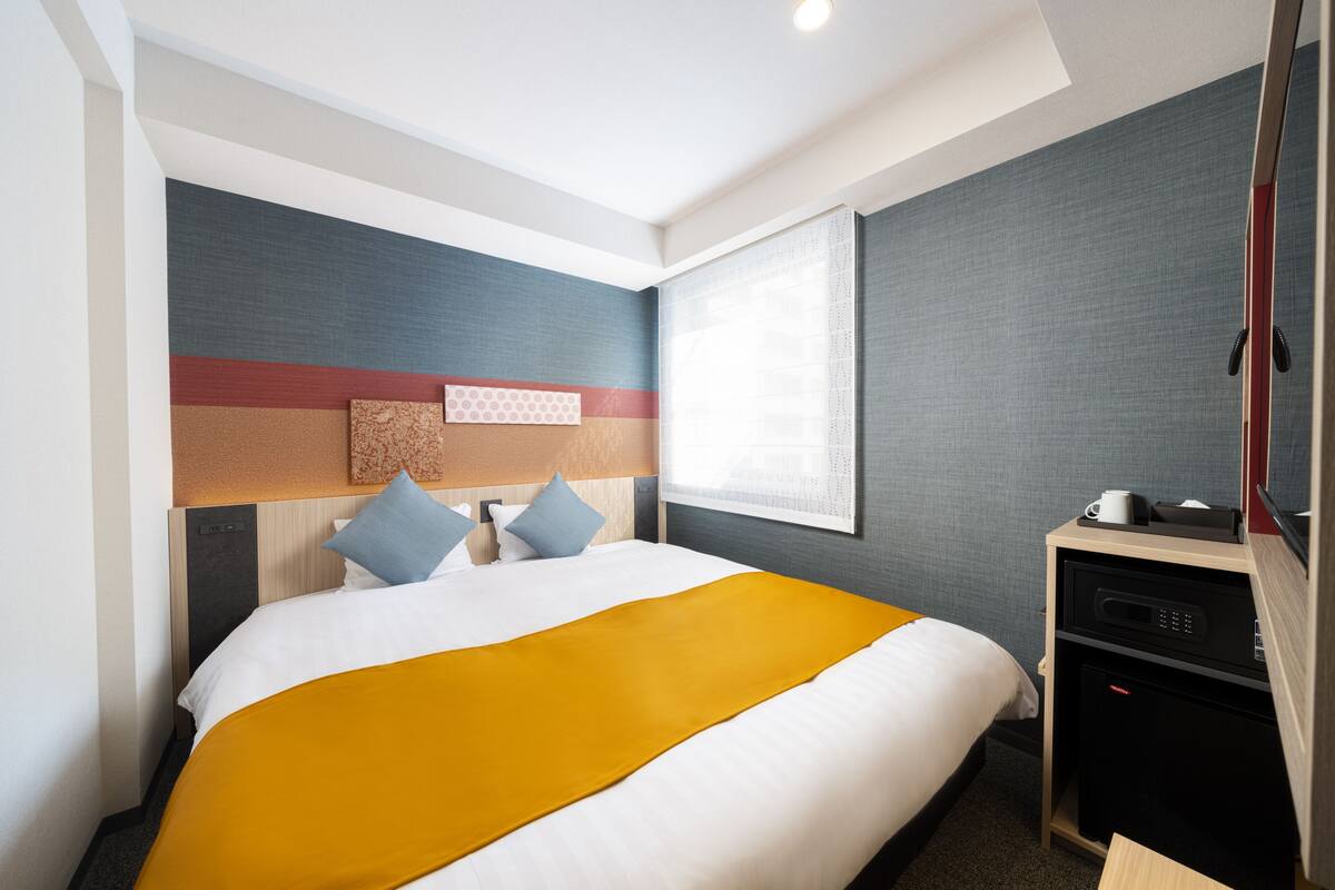 Une chambre d’hôtel comprenant un lit, un bureau, une chaise, une fenêtre et un mur au décor texturé.