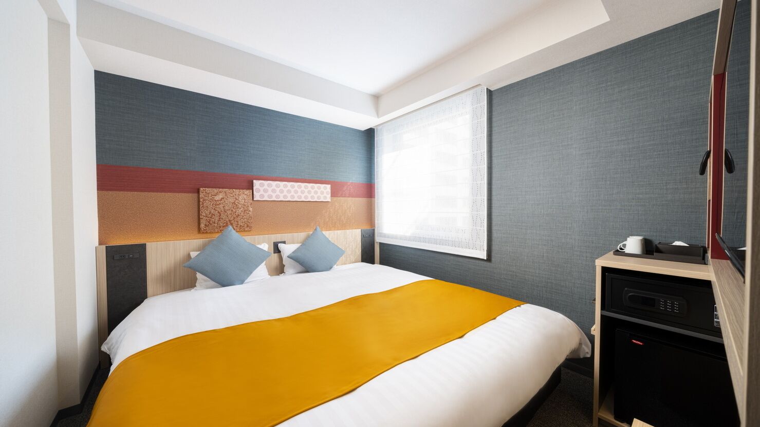 Une chambre d’hôtel avec un lit, un bureau, une fenêtre et un mur au décor texturé.