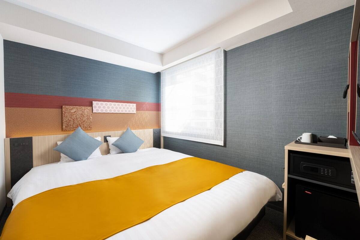 Une chambre d’hôtel avec un lit, un bureau, une fenêtre et un mur au décor texturé.