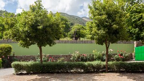 A landscaped garden with trees, a stone wall, and a green fence. - Villas Arhontika Red, Nestled in Chestnut Forest in Cretan Mountainside (Elos)