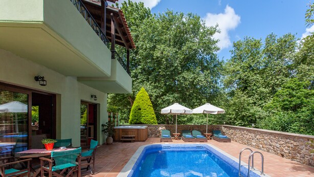 A swimming pool with a stone wall and a wooden deck. There are chairs and umbrellas. - Villas Arhontika Red, Nestled in Chestnut Forest in Cretan Mountainside (Elos)