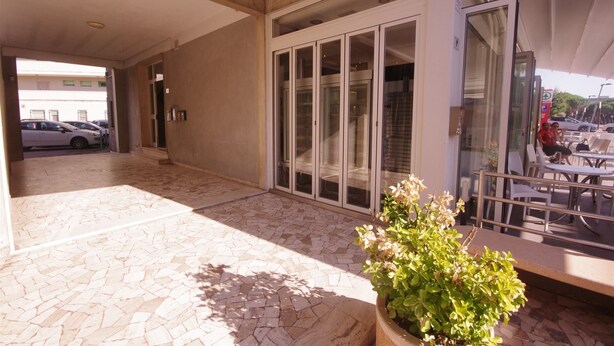 Un espace extérieur abrité, doté d’un sol carrelé, d’une plante en pot et d’une porte vitrée donnant sur un espace intérieur.