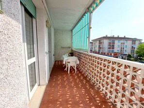 A balcony with a tiled floor, a table with chairs, and a view of buildings in the background. - Serena 2-9: Two-room apartments in the city center, with air conditioning and a large terrace (Comacchio)