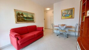 Un salon avec un canapé rouge, une table à manger entourée de chaises et deux tableaux encadrés accrochés aux murs.