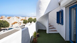 A white building with blue shutters, a green artificial lawn, and a view of other buildings in the distance.