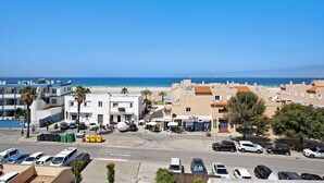 A coastal town with a beach, buildings, and parked cars.