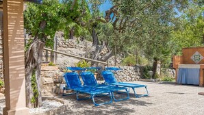 A patio area with blue lounge chairs, a stone wall, and a pergola with climbing plants.