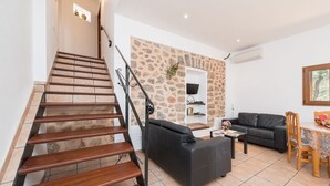 A staircase with wooden steps and metal railings, a black leather sofa, a coffee table, a stone-patterned wall, and a television on a shelf.