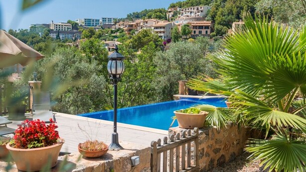 A swimming pool with a stone wall, potted plants, and a lamp post.