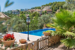 A swimming pool with a stone wall, potted plants, and a lamp post.