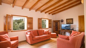 Ein Wohnzimmer mit Holzbalkendecke, einer Couch, einem Fernseher und Fenstern mit Holzläden.