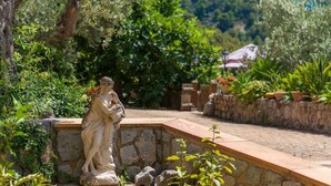 Ein Garten mit Steinmauer, Statue und verschiedenen Pflanzen.