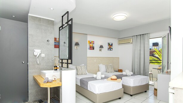 A hotel room with two beds, a bathroom with a shower, and a small desk with a mirror. - Icandy Malia (Hersonissos)