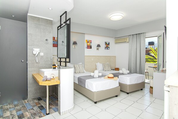 A hotel room with two beds, a bathroom with a shower, a vanity with a mirror, and artwork on the walls. - Icandy Malia (Hersonissos)