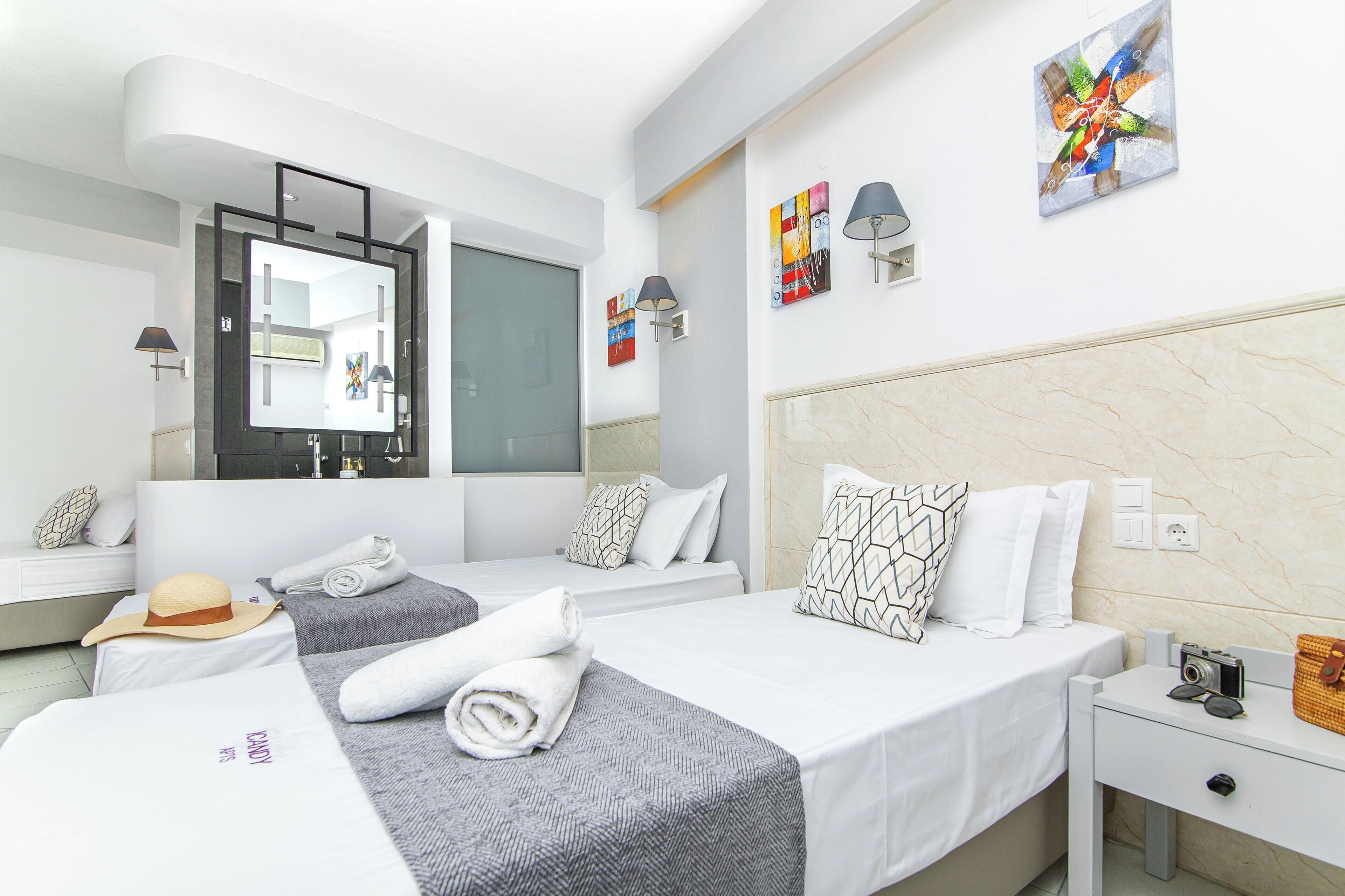 A modern hotel room with two beds, a large mirror, artwork on the walls, and a small table with a camera and a handbag.