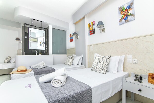 A modern hotel room with two beds, a large mirror, artwork on the walls, and a nightstand with a camera and sunglasses. - Icandy Malia (Hersonissos)