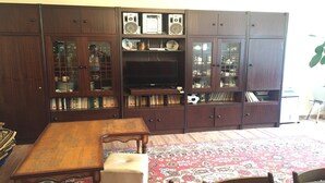 Un salon traditionnel avec un meuble de rangement en bois servant de support pour l’équipement audiovisuel, un téléviseur et une table à manger.