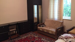 Une pièce avec un meuble en bois, un canapé, un tapis à motifs et une fenêtre avec des rideaux.