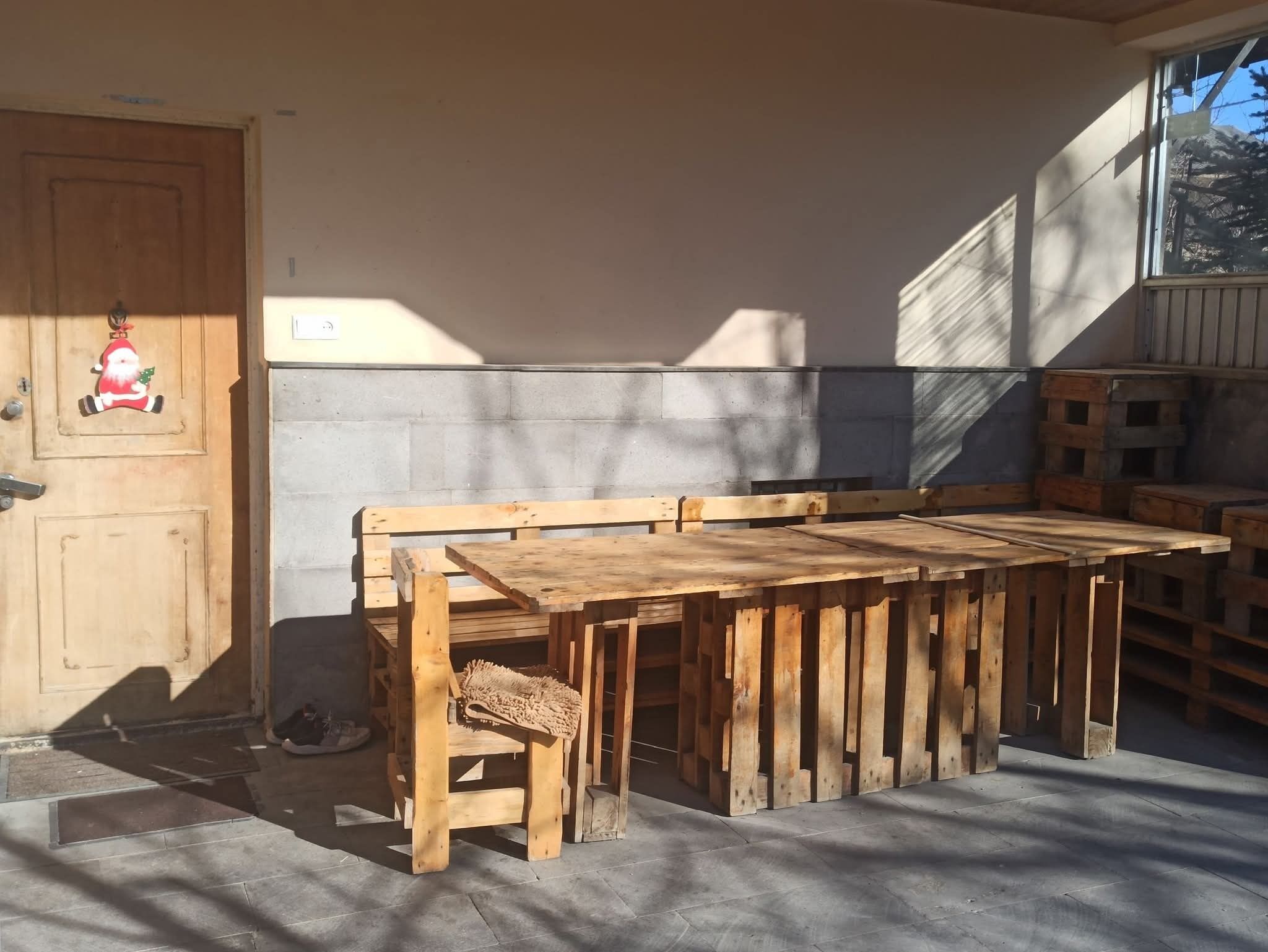 Un banc et une table en bois sont installés à l’extérieur d’un bâtiment doté d’un mur en béton et d’une porte en bois décorée d’un motif représentant le Père Noël.