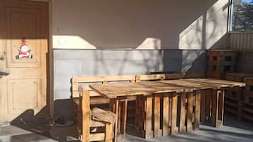 Un banc et une table en bois sont installés à l’extérieur d’un bâtiment doté d’un mur en béton et d’une porte en bois décorée d’un motif représentant le Père Noël.