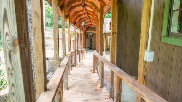 Ein gedeckter Holzsteg mit Geländer, der zu einem Gebäude mit grünem Fensterrahmen führt.