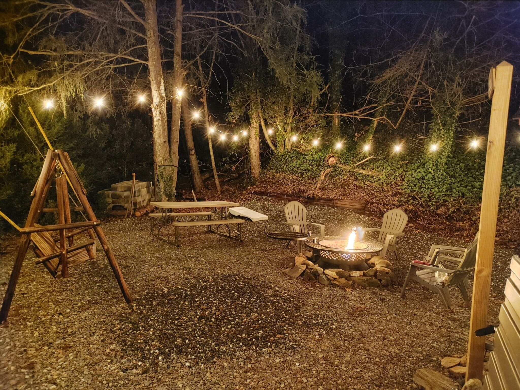 An outdoor patio area with a swing set, picnic table, chairs, and a fire pit.