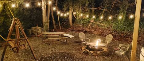 An outdoor patio area with a swing set, picnic table, chairs, and a fire pit.