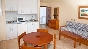 Un espacio habitable compacto con kitchenette, una mesa de comedor con sillas, un sofá y un cuadro en la pared.