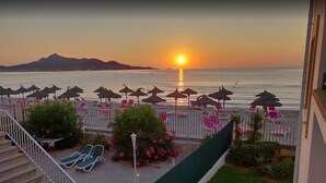Vista de una playa con agua iluminada por el sol, sillas de descanso y sombrillas.