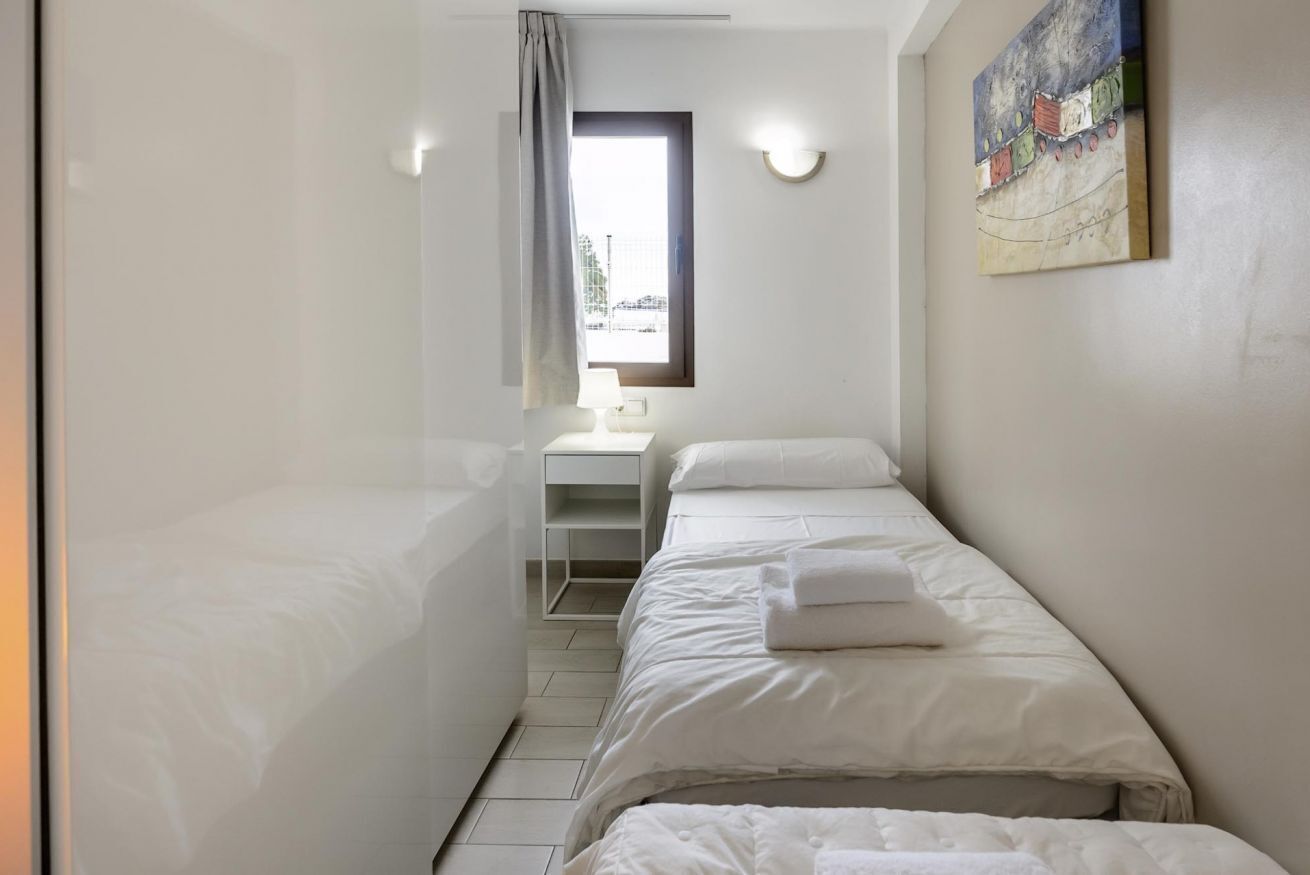 Una habitación de hotel pequeña y moderna, con dos camas individuales, un escritorio con una silla, una ventana con cortinas y un cuadro en la pared.
